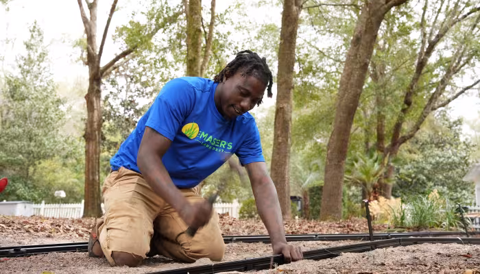 Landscape installation team member securing edging along a new garden pathway in a wooded backyard.