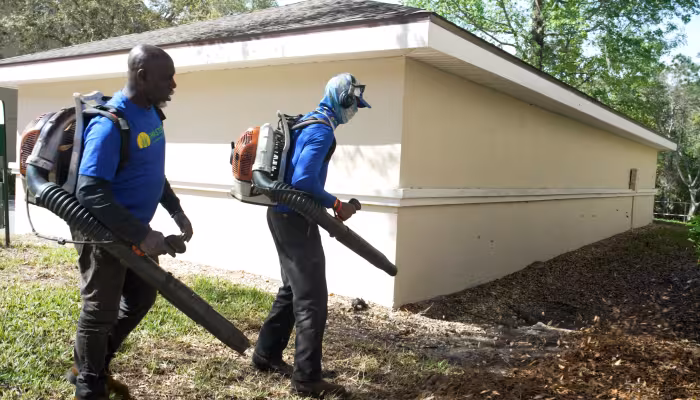 Two landscape maintenance team members using backpack blowers to clear debris around a condominium building.