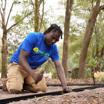 Landscape installation team member securing edging along a new garden pathway in a wooded backyard.