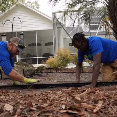 Two landscape professionals installing pathway edging as part of a backyard landscape renovation project.