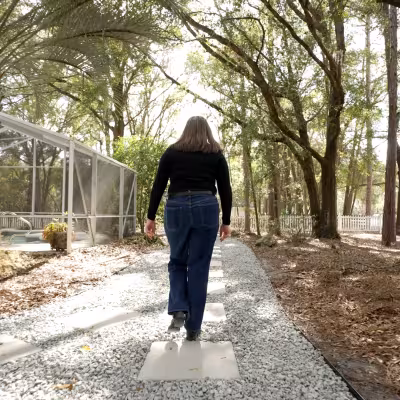 Homeowner walking along a newly completed stone pathway connecting outdoor living spaces in a landscaped backyard.