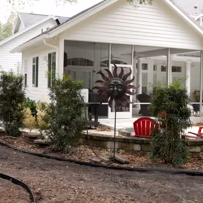 Landscape professionals preparing a custom pathway route through a wooded backyard near a screened pool enclosure.