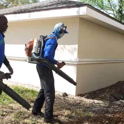 Two landscape maintenance team members using backpack blowers to clear debris around a condominium building.