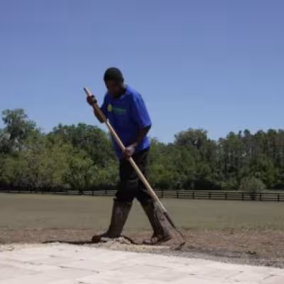 Landscape team member grading and preparing soil along the driveway during the lawn renovation.