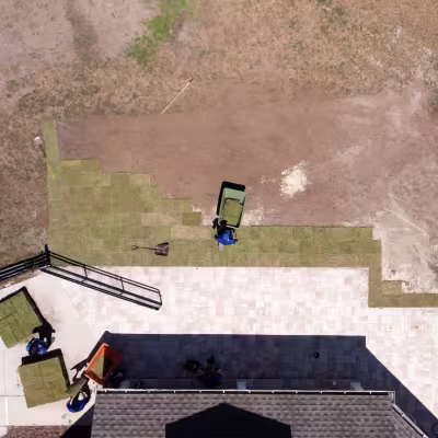 Aerial view of the crew installing new sod around the completed paver patio and walkway.