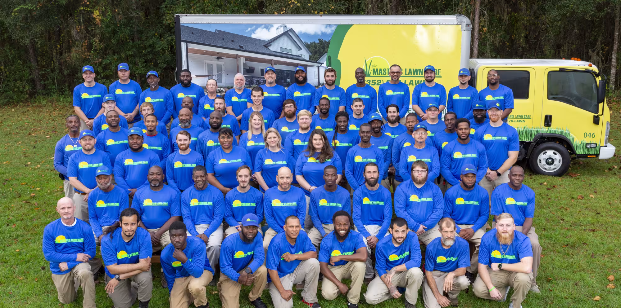TMLC company photo showing everyone lined up in neat rows with blue shirts in front of a company truck