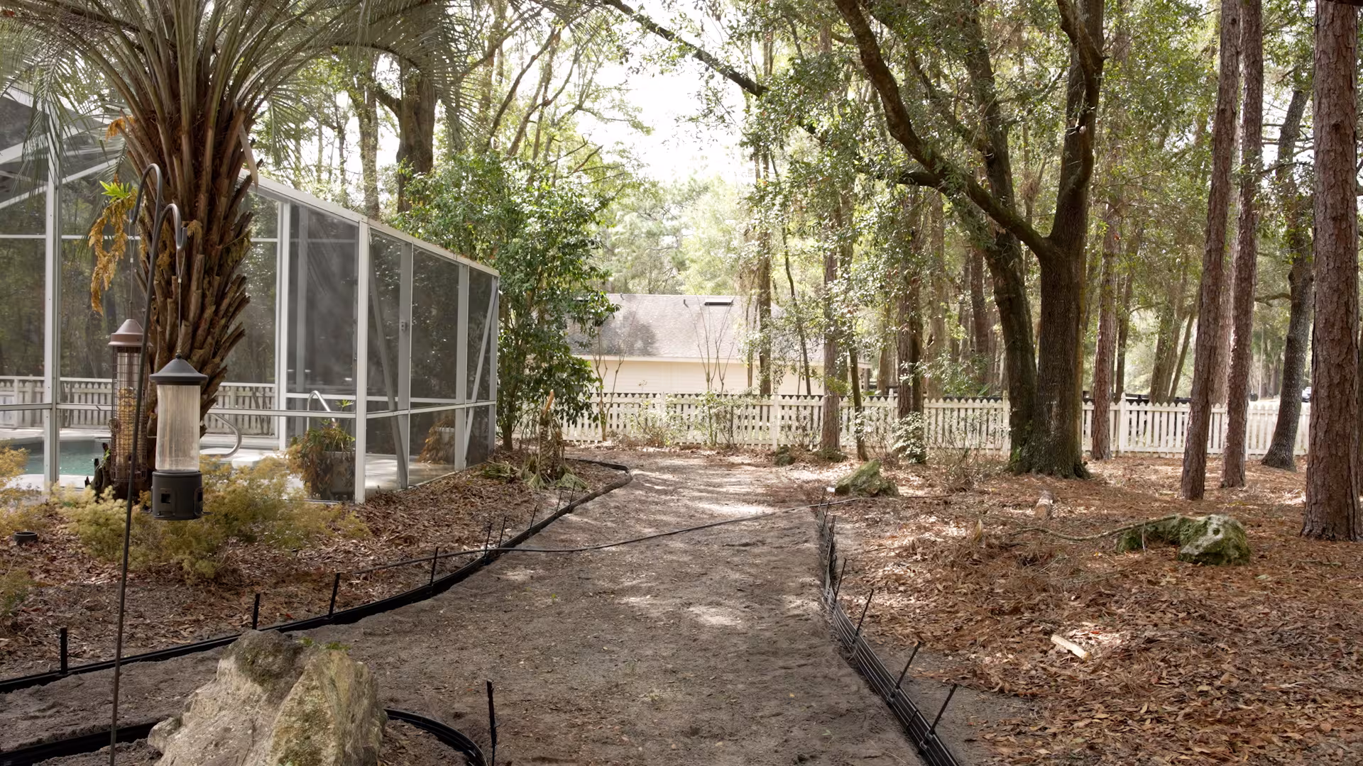 Before photo of a wooded backyard with a dirt pathway route and minimal connection between the pool area and surrounding outdoor spaces.