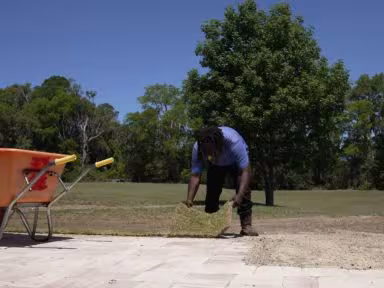 Landscape team member preparing soil beside the driveway during sod installation at a Gainesville home.